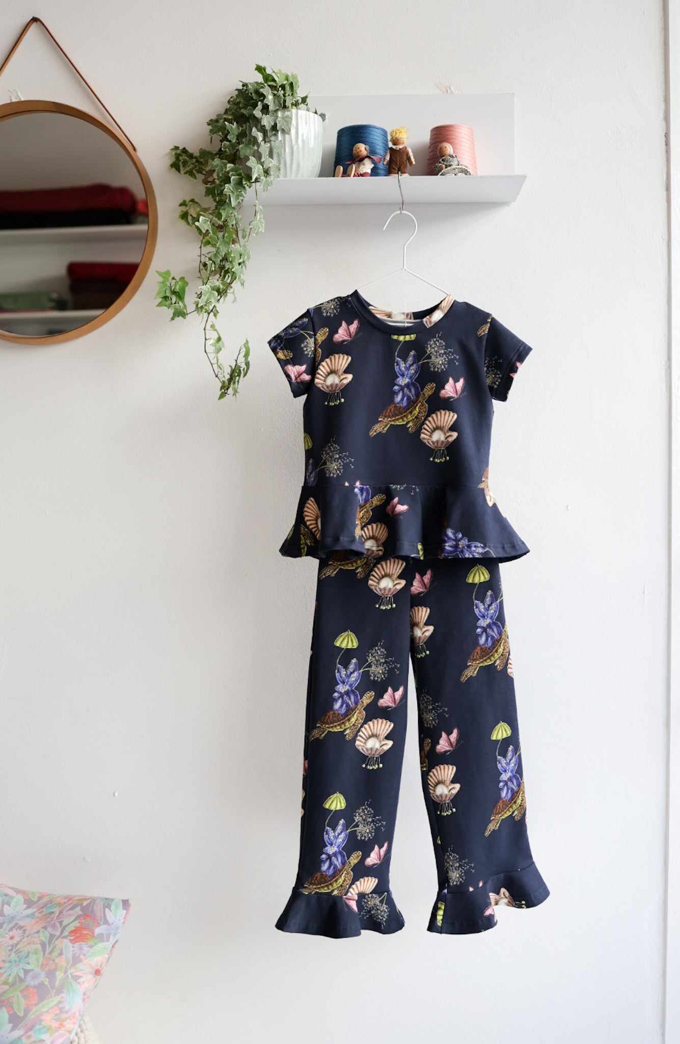 Navy blue kids top and pants with colorful print hanging on a white wall.