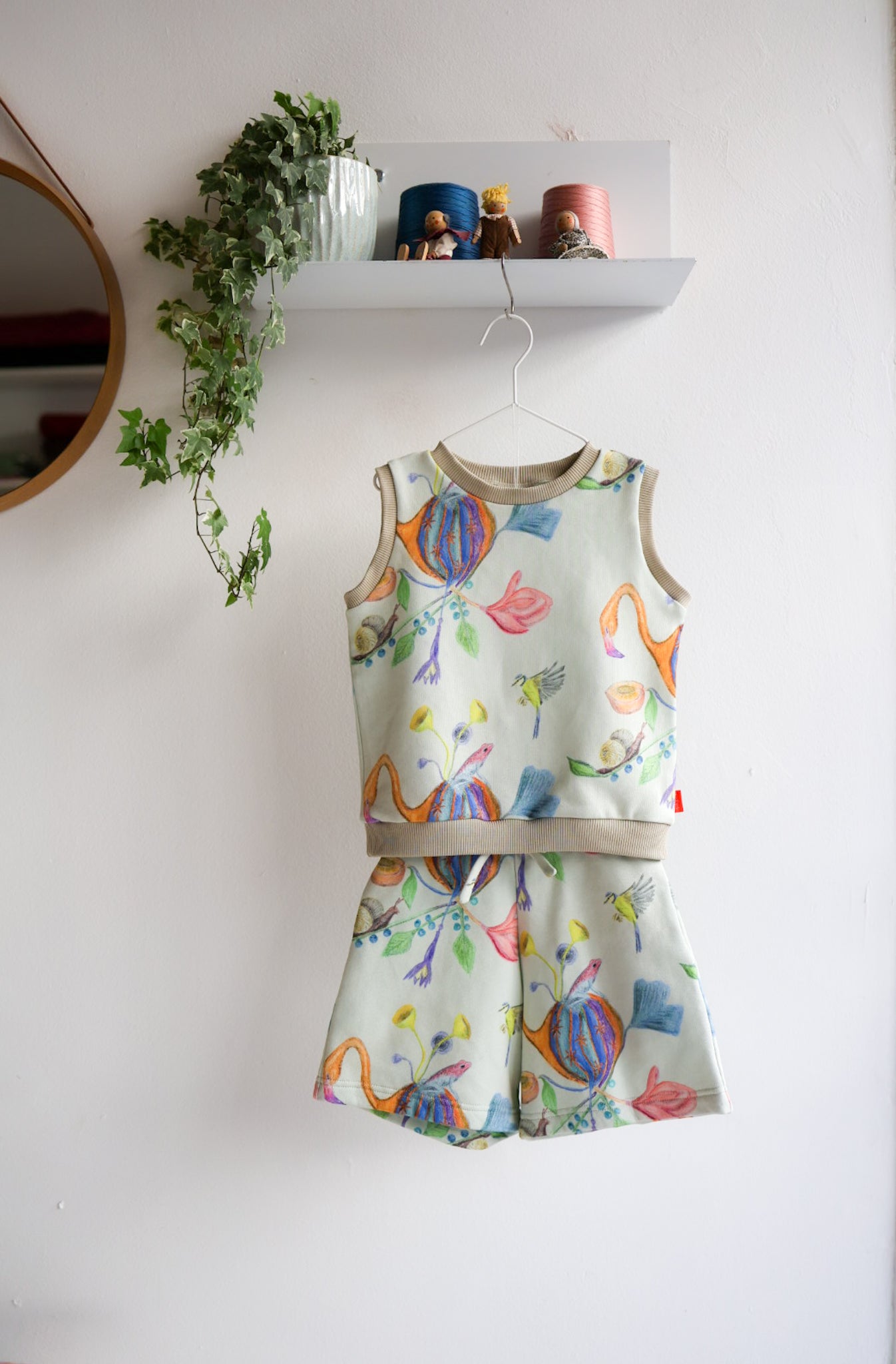 Children's sleeveless top and shorts set with colorful designs on a white wall.