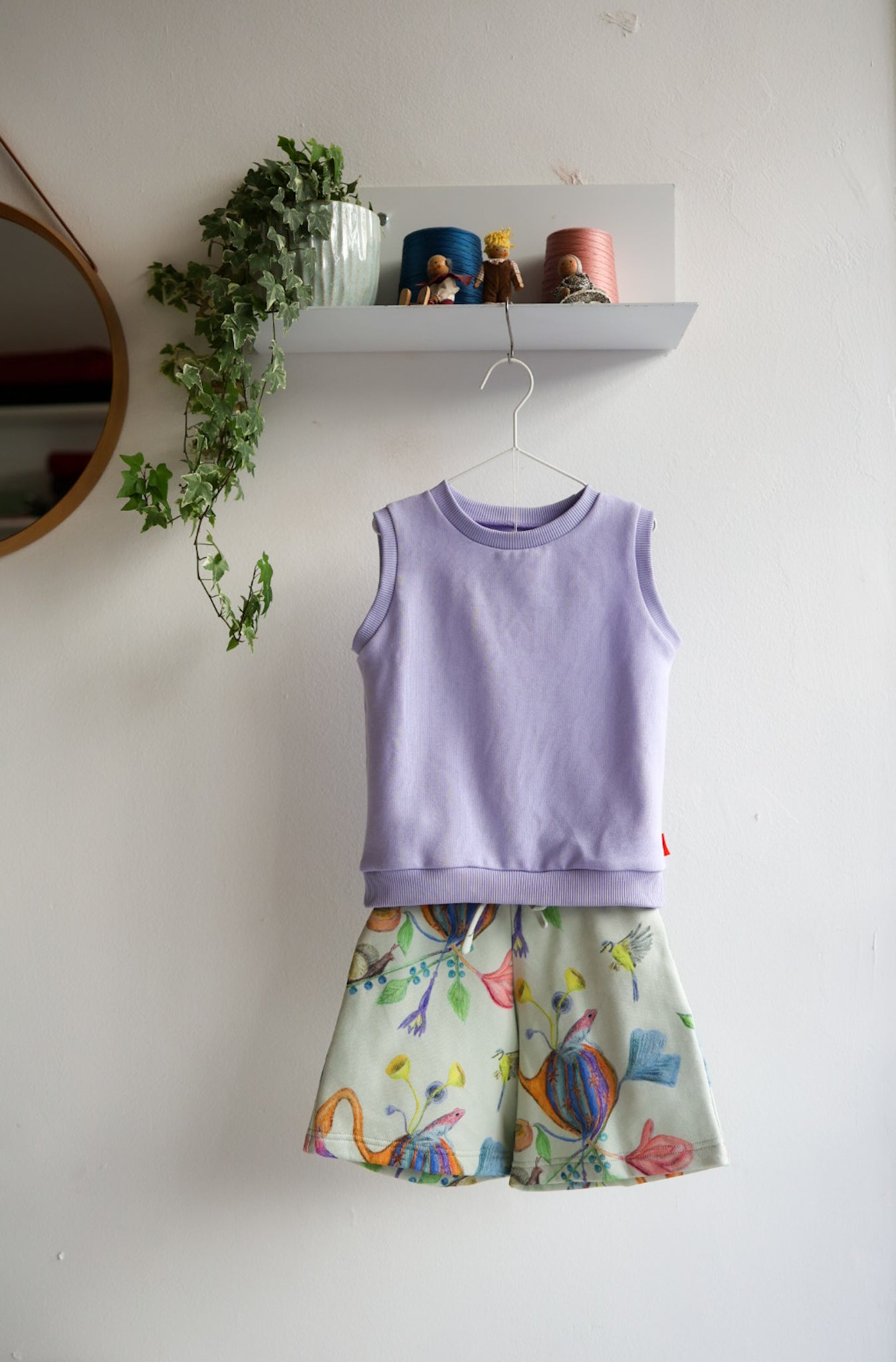 Lavender kids sleeveless top and colorful shorts hanging on a white wall.