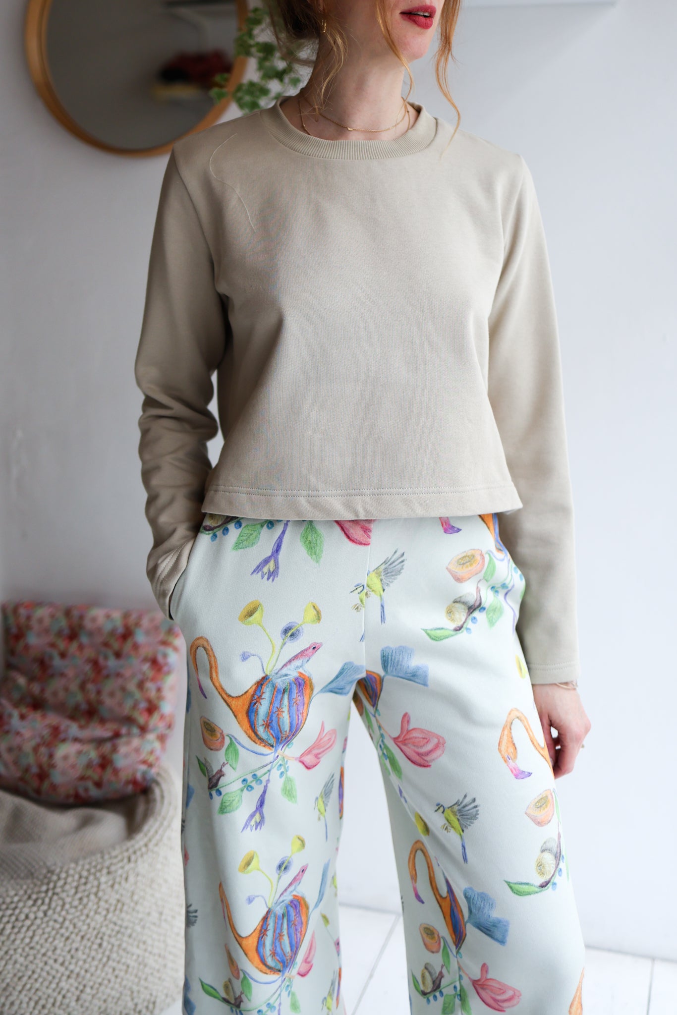 Person wearing a beige long-sleeve top and colorful pants with a white background