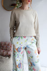 Person wearing a beige long-sleeve top and colorful pants with a white background