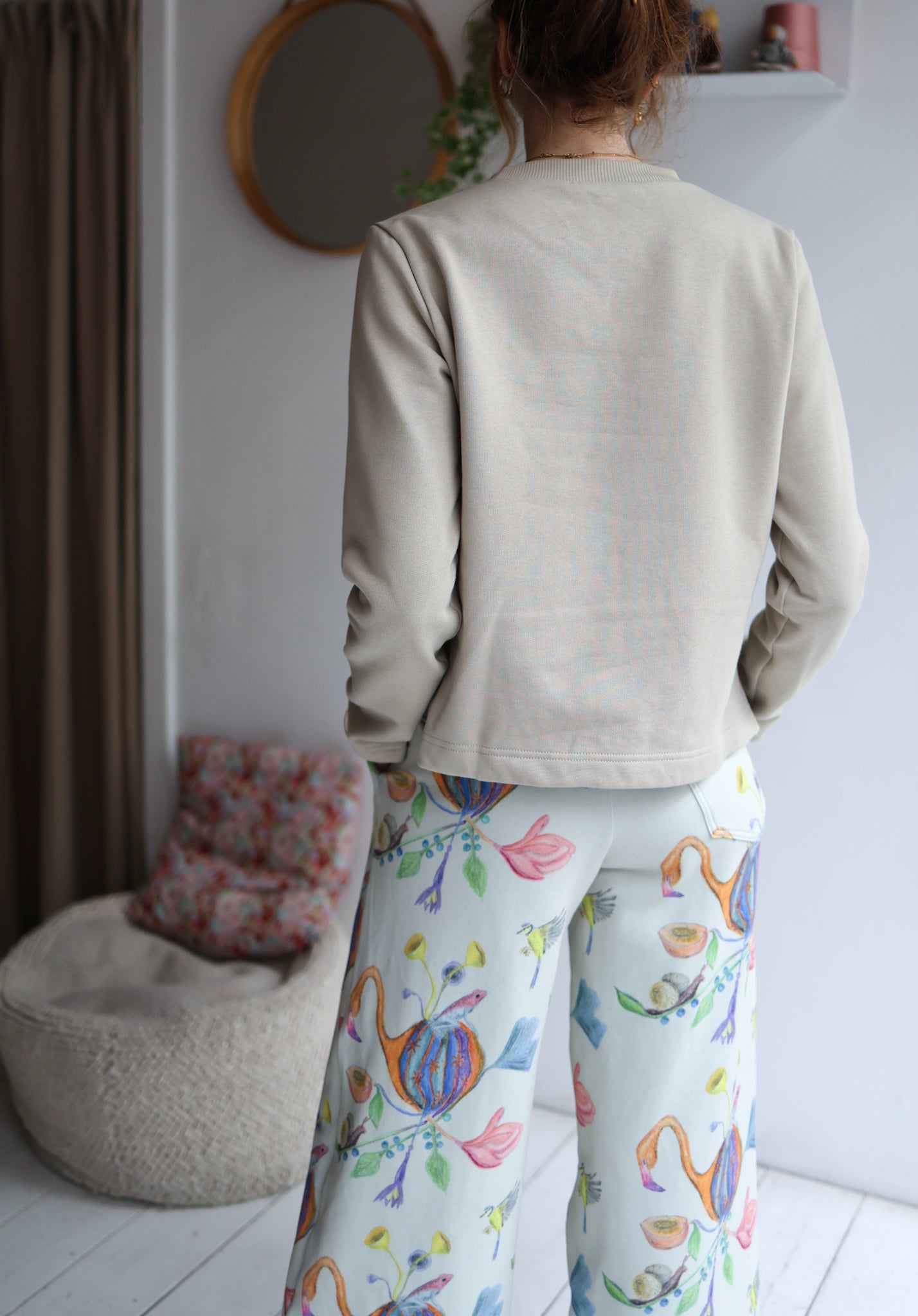 Person wearing a beige sweater and colorful patterned pants in a room with a mirror and bean bag chair.