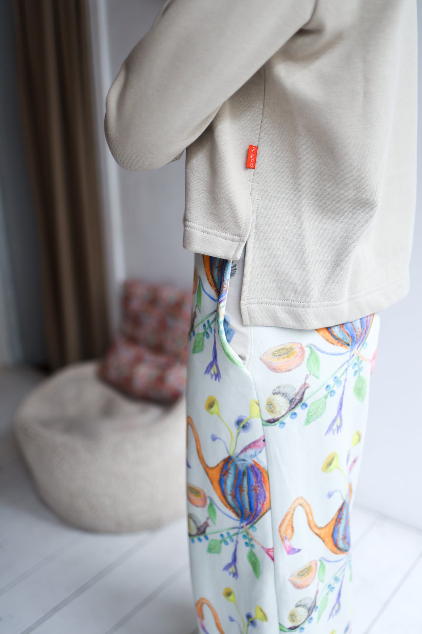 Person wearing a beige jacket and colorful dinosaur-patterned pants indoors.