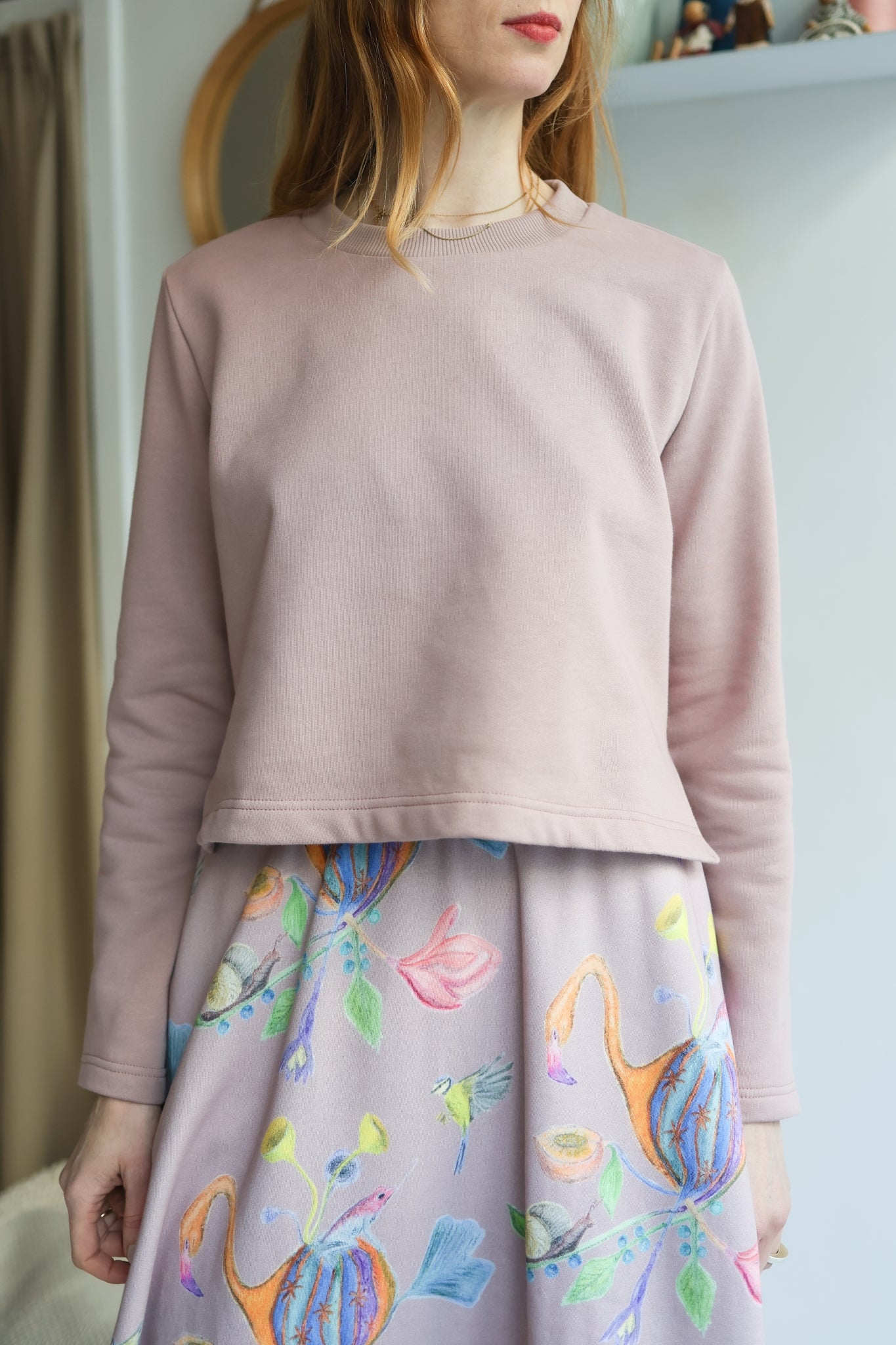 Person wearing a light pink sweater and colorful skirt indoors.