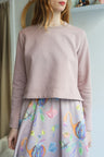 Person wearing a light pink sweater and colorful skirt indoors.