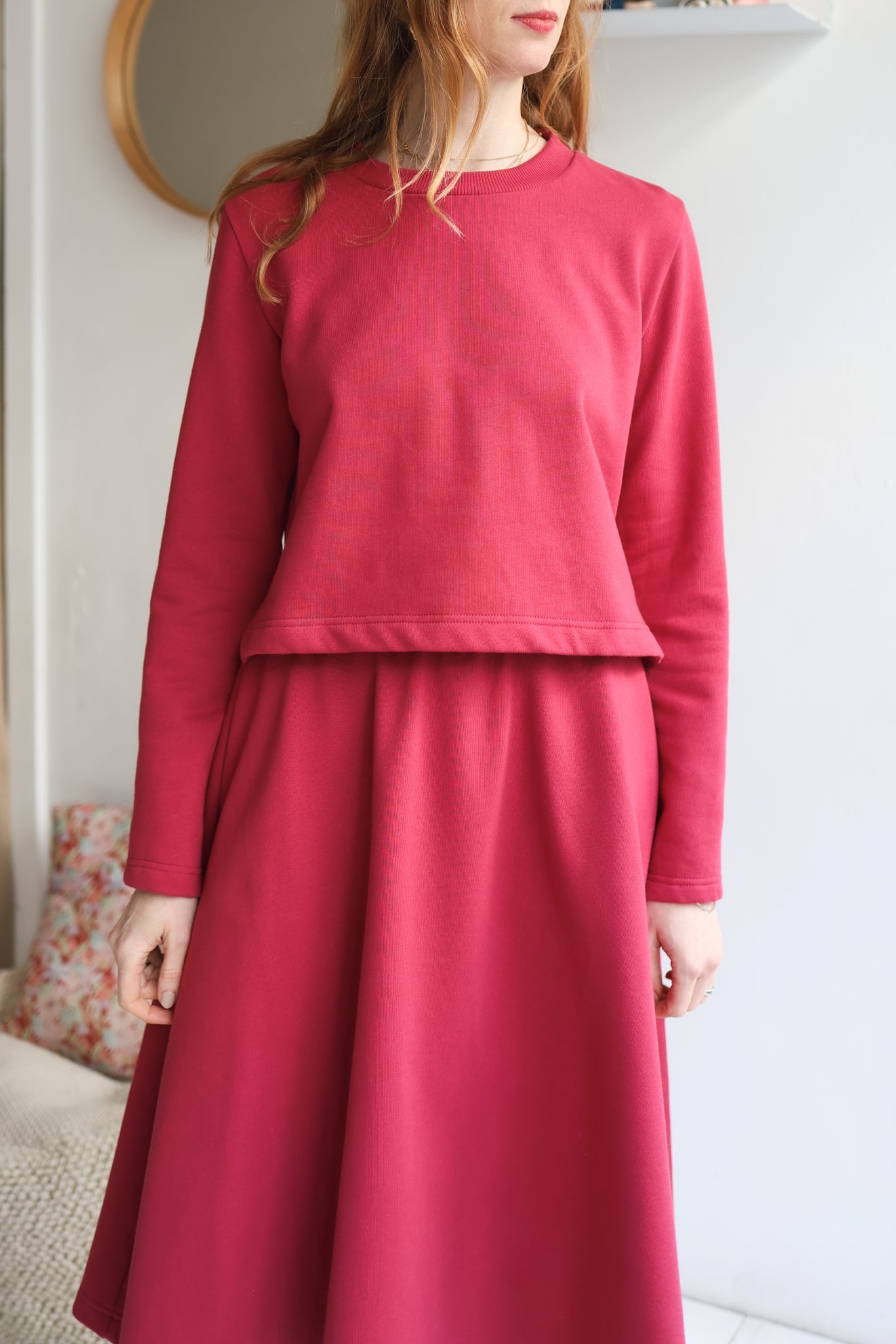 Person wearing a red outfit standing against a white wall.