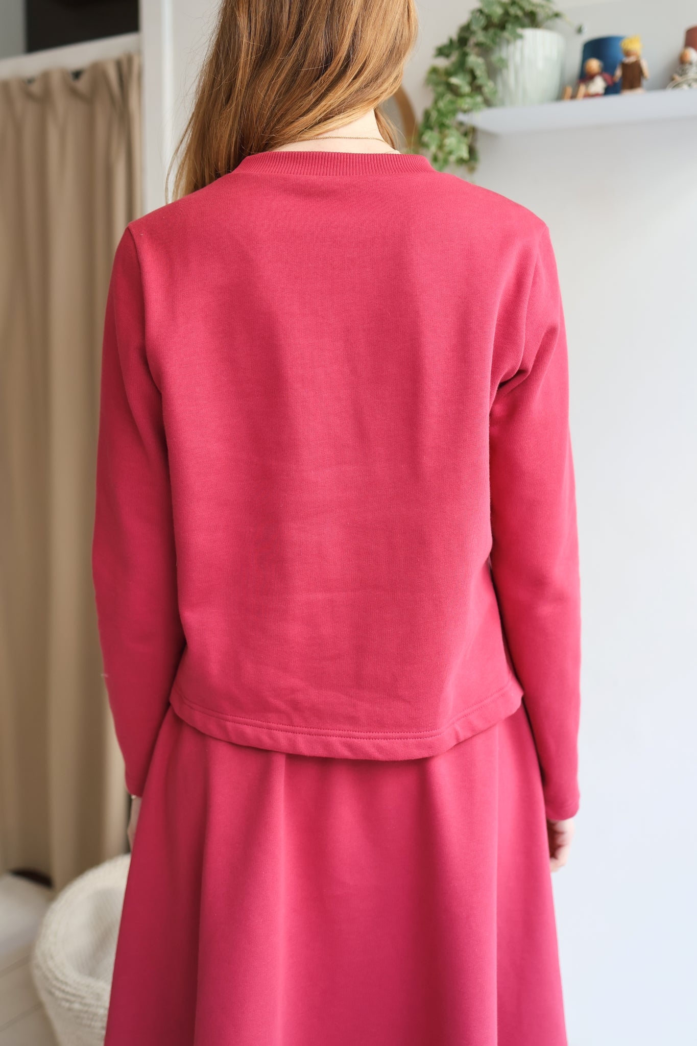 Person wearing a pink outfit in a room with a white wall and some decor items.